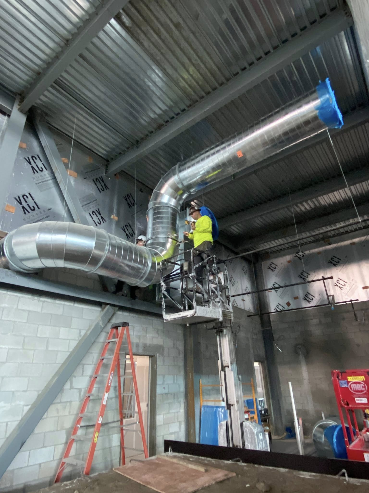 CFM technician on a boom lift connecting spiral duct elbows to a rooftop unit