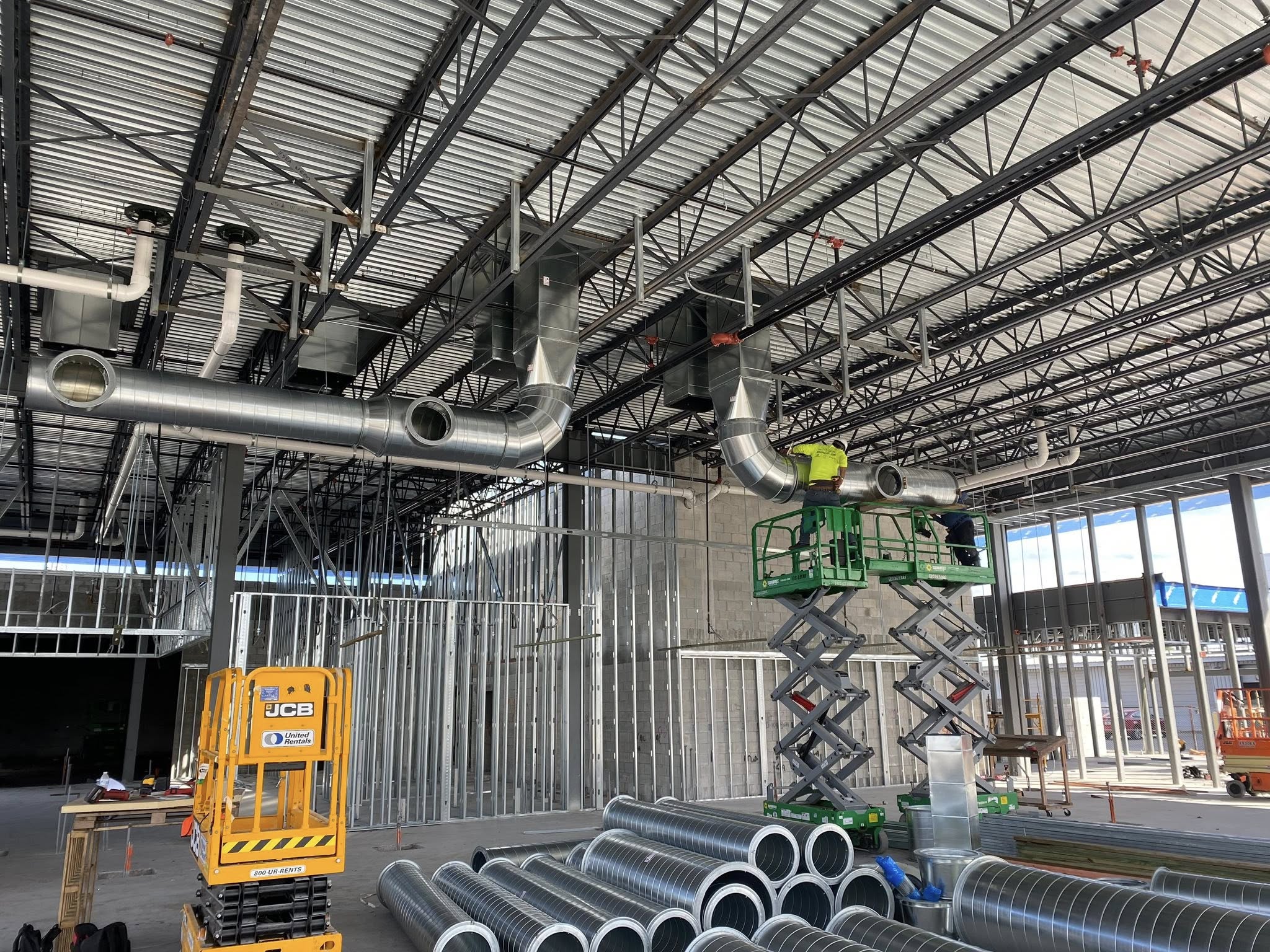 CFM crew installing large spiral supply ductwork from a scissor lift in a high-bay warehouse