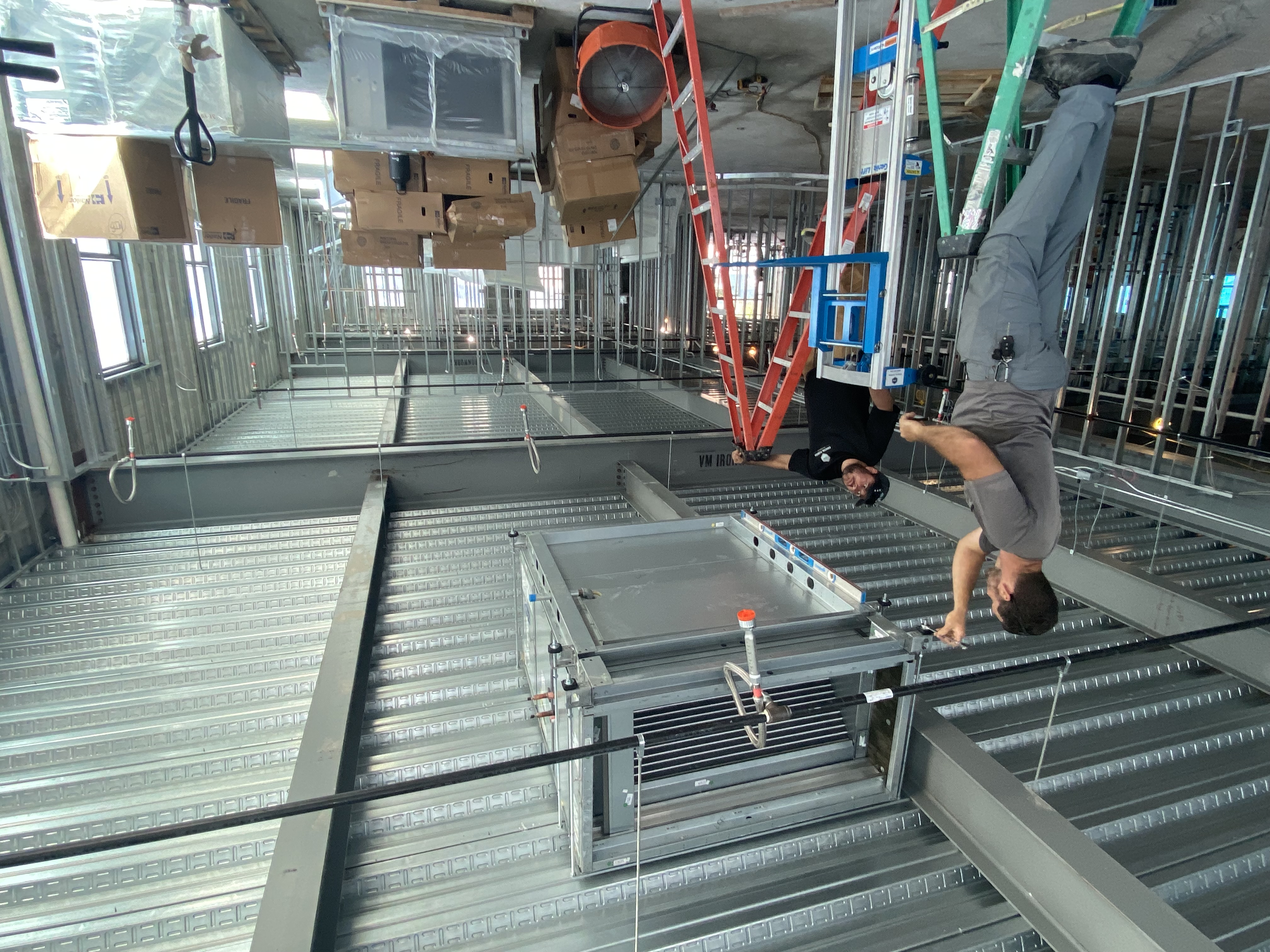 CFM crew installing a packaged HVAC unit overhead from ladders on a jobsite